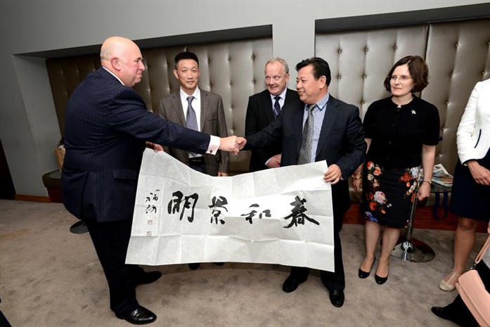 Picture of a group of men and women holding a large banner with Chinese writing on it, shaking hands