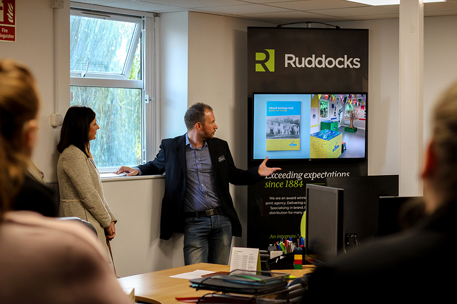 Man standing in front of TV screen and Ruddocks branded stand, people watching him