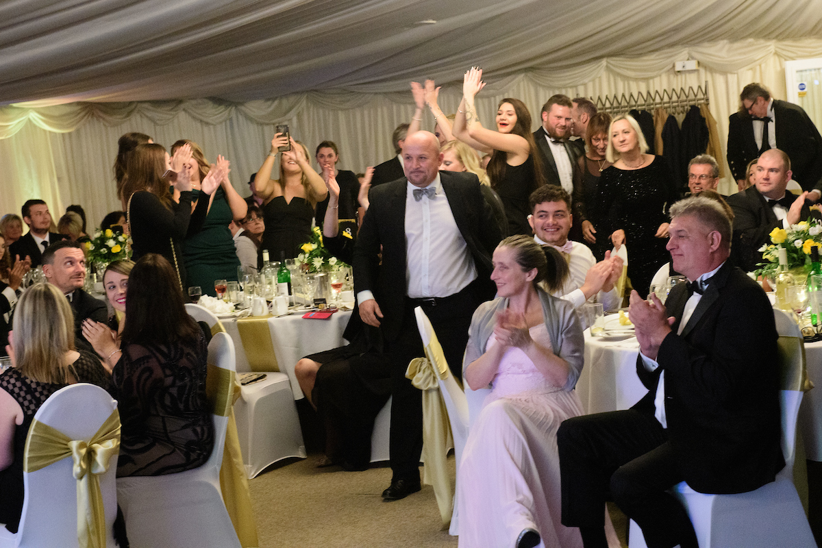 Group of people in formal eveningwear, some standing and seating, cheering and clapping