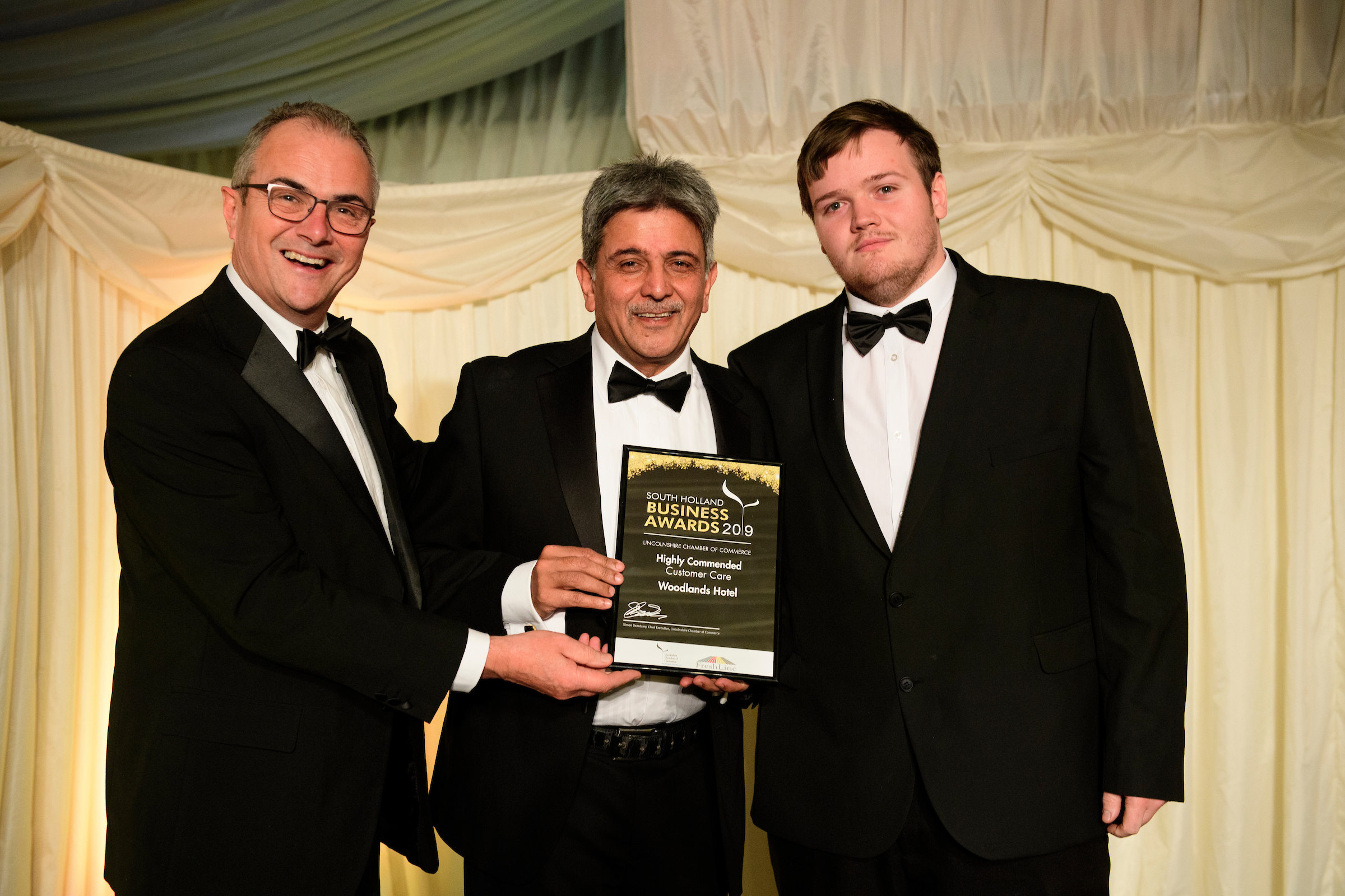 Three men in formal evening wear holding trophies and certificates and smiling at the South Holland Business Awards 2019