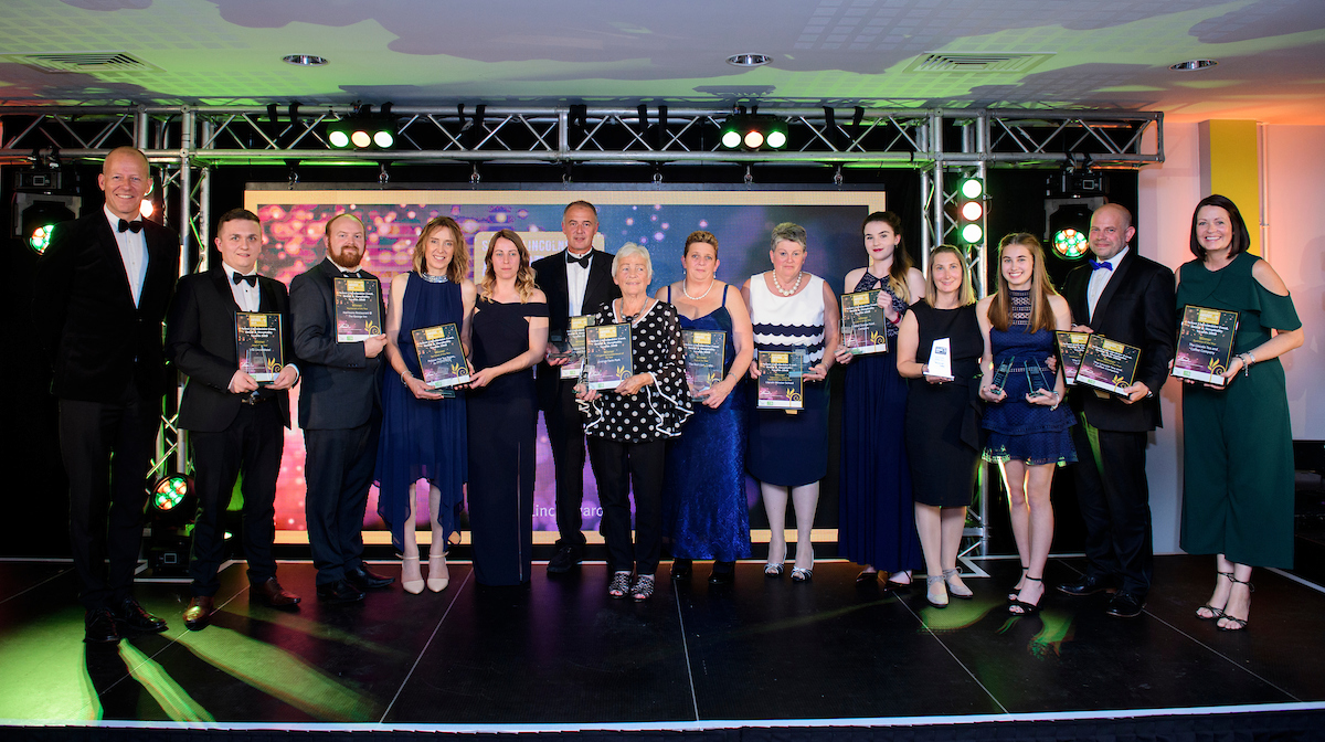 Group of people wearing formal evening wear and holding certificates and trophies at an award show