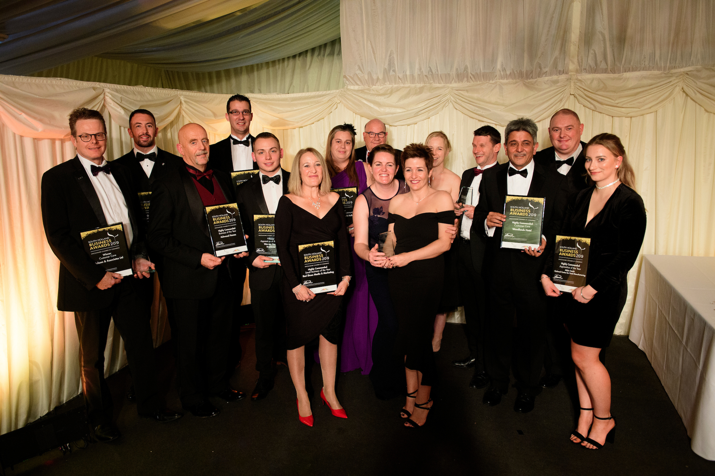 Group of people in eveningwear holding framed certificates, trophies, posing and smiling at the South Holland Business Awards 2019