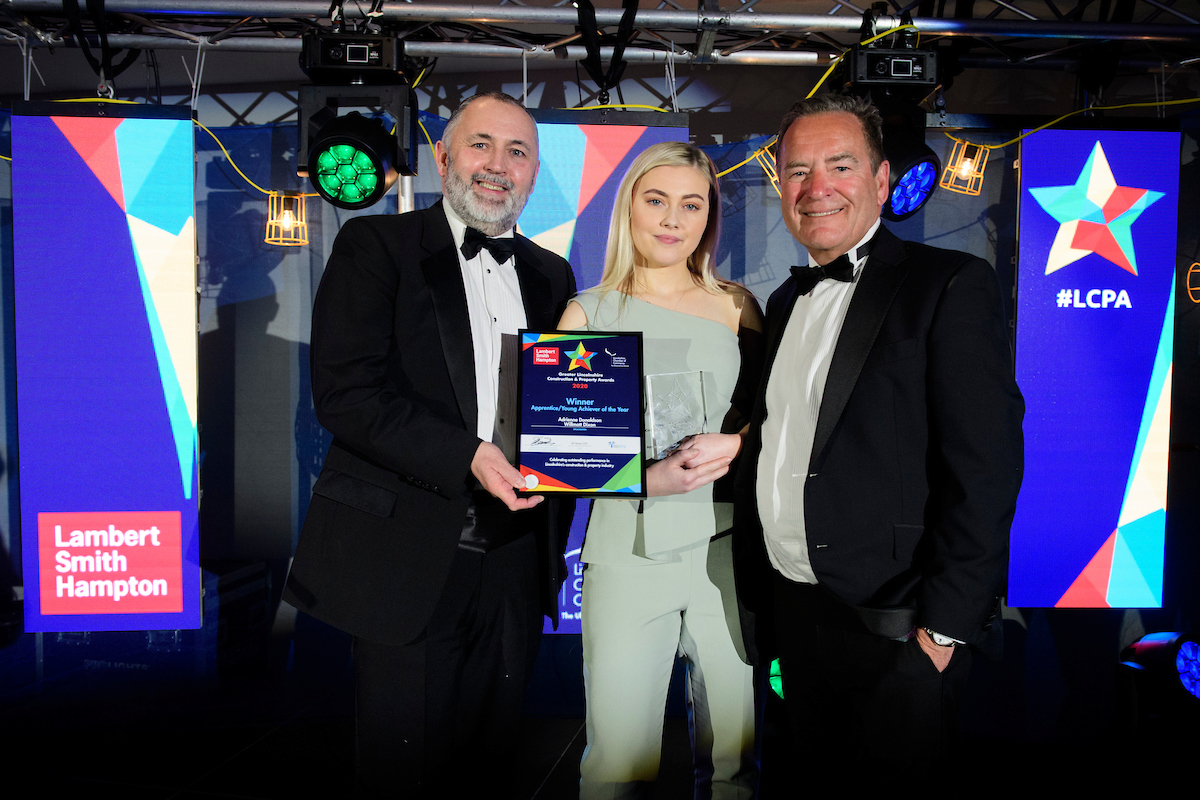 Two men and a young woman at an awards show, holding a certificate