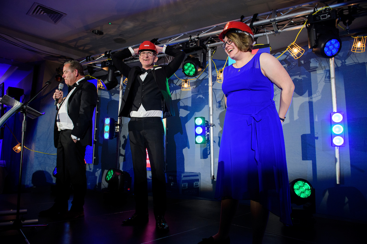 Woman with blue dress wearing a red hard hat and man with suit on stage at The Greater Lincolnshire Construction and Property Awards 2020 with host Jeff Stelling