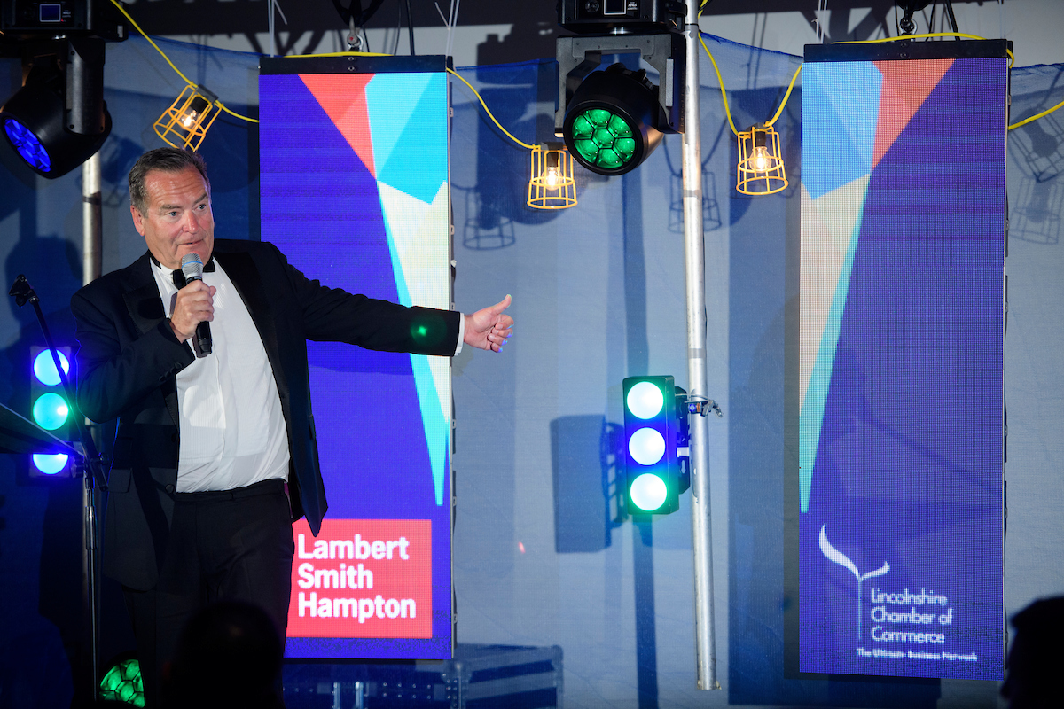 Greater Lincolnshire Construction & Property Awards 2020 host Jeff Stelling on stage with microphone and Lincolnshire Chamber of Commerce logo