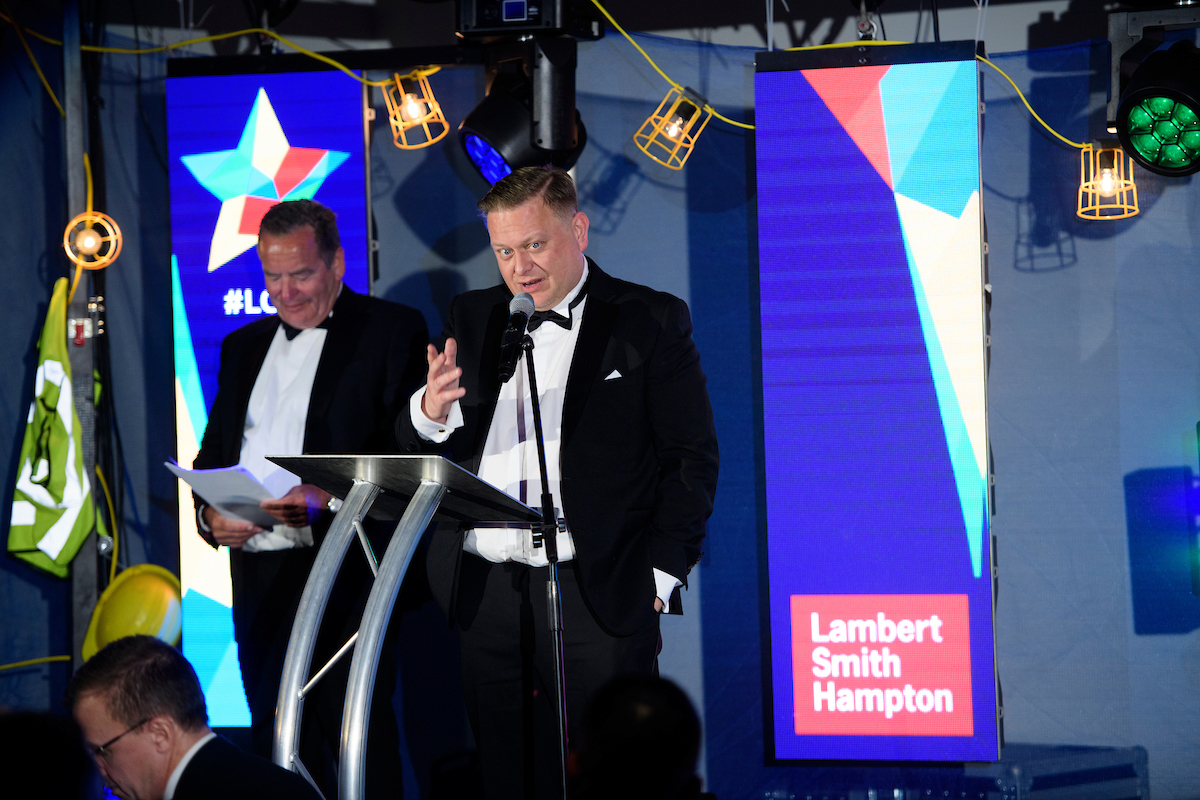 Two men on stage at an awards show with tv screen in the background