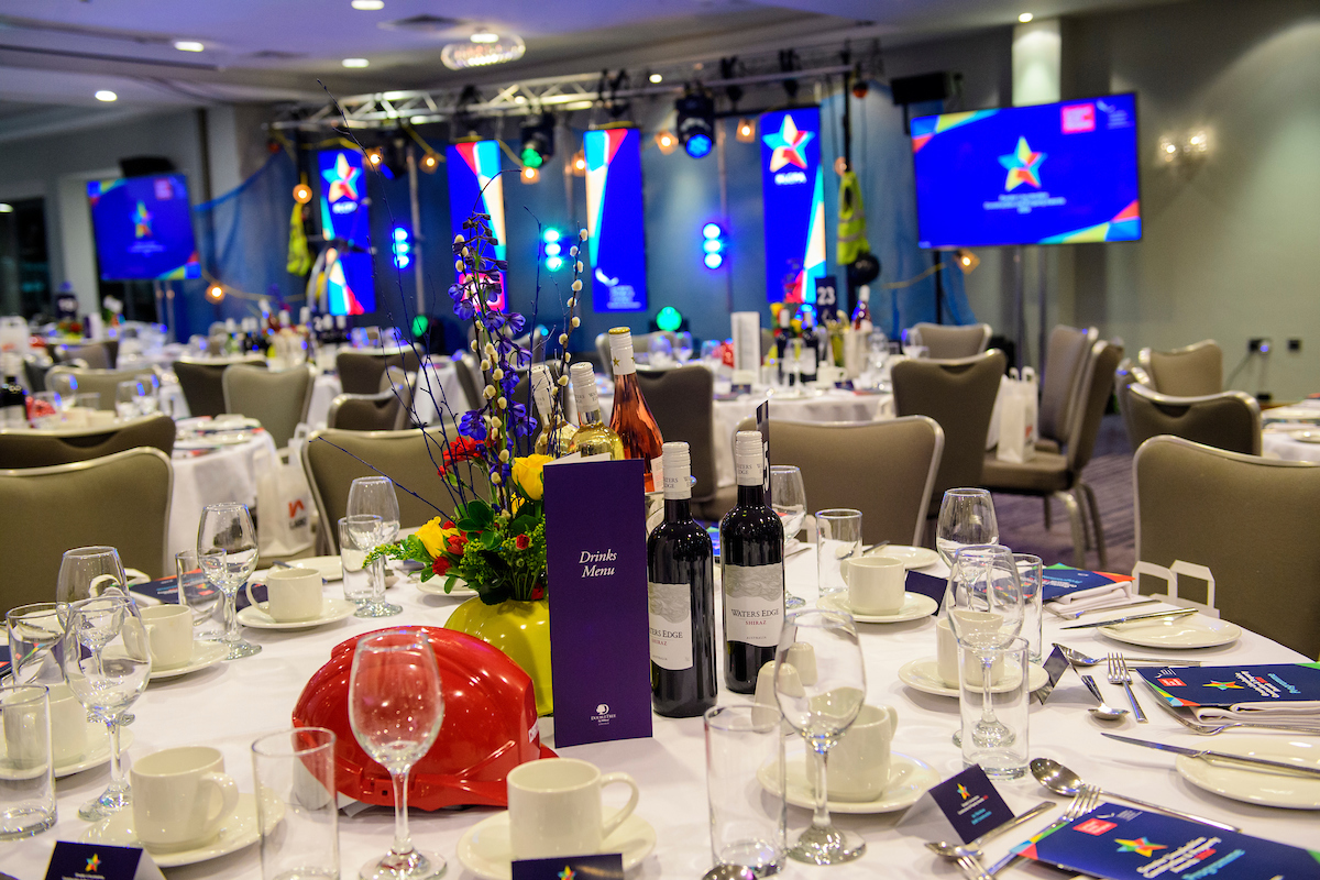 Set up of an awards dinner, picture of a table with glasses, plates, cutlery, a red hard hat and flower arrangement at The Greater Lincolnshire Construction and Property Awards 2020