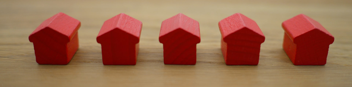 Five miniature red houses from a Monopoly game in a row on wooden table