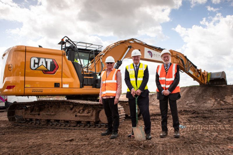 Three men in high visibility jackets and hard hats posing with construction machinery