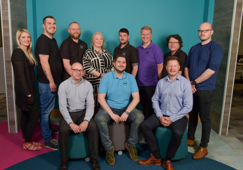 Group of men and women sitting and standing in front of bright blue wall