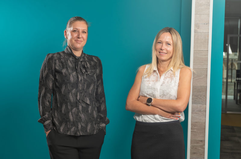 Man and woman posing and smiling in front of bright blue wall