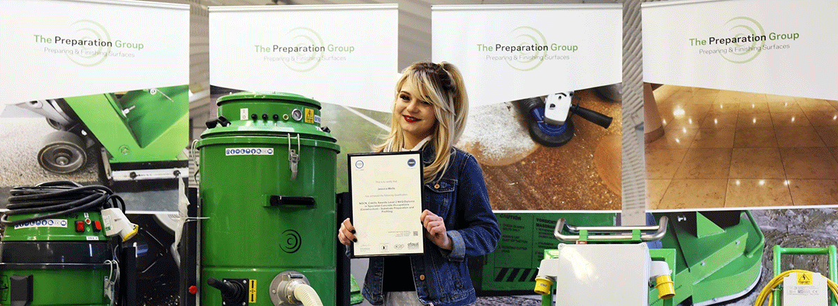 Young blonde woman holding certificate surrounded by green heavy machinery