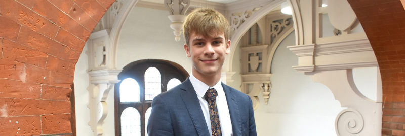A young man in blue suit and tie posing inside the Lincoln UTC building