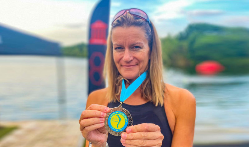 Blonde woman holding a medal with blue ribbon in front of lake
