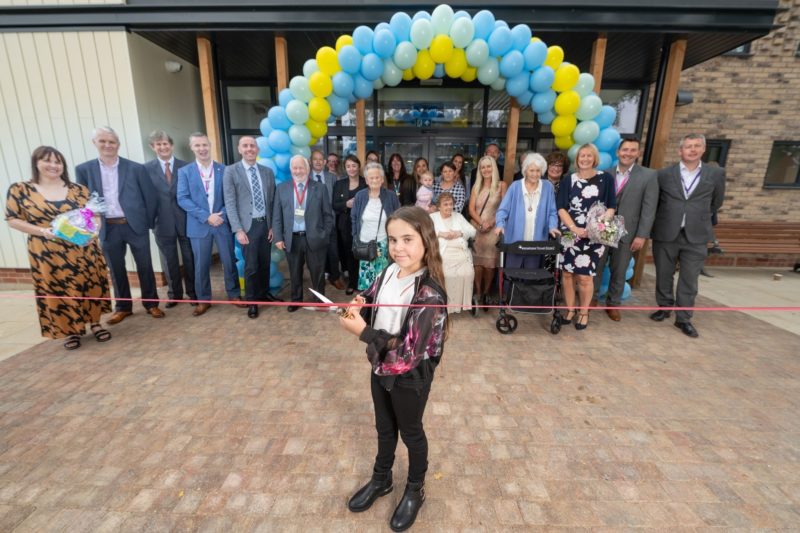 Young girl cutting red ribbon in front of Balloon archway made of yellow and blue balloons, opening Myos House in Scunthorpe