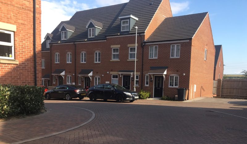 Several blocks of flats with grey roof and red bricks on a street