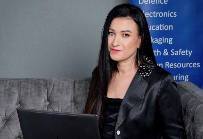 Dark haired woman wearing black with laptop on grey sofa