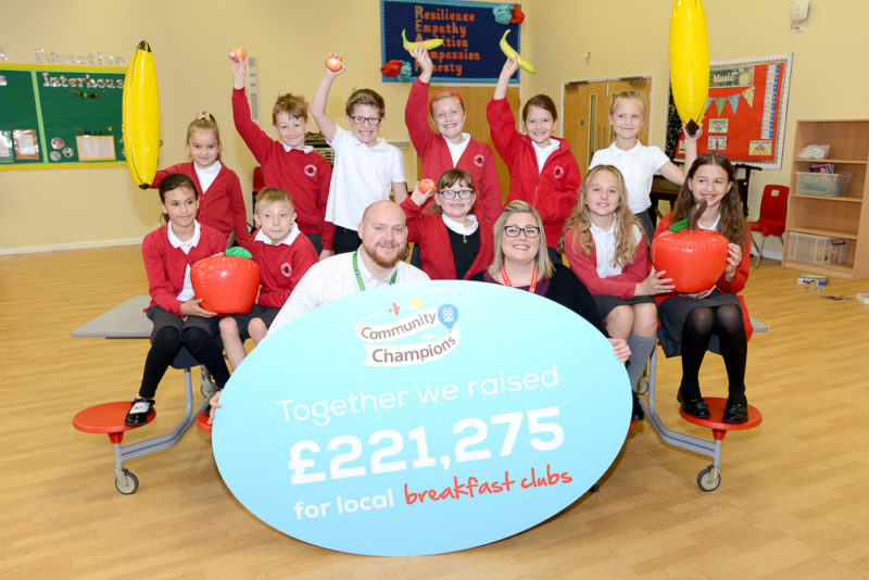 Children in red jumper school uniforms, a man and woman holding a blue board with fundraising information