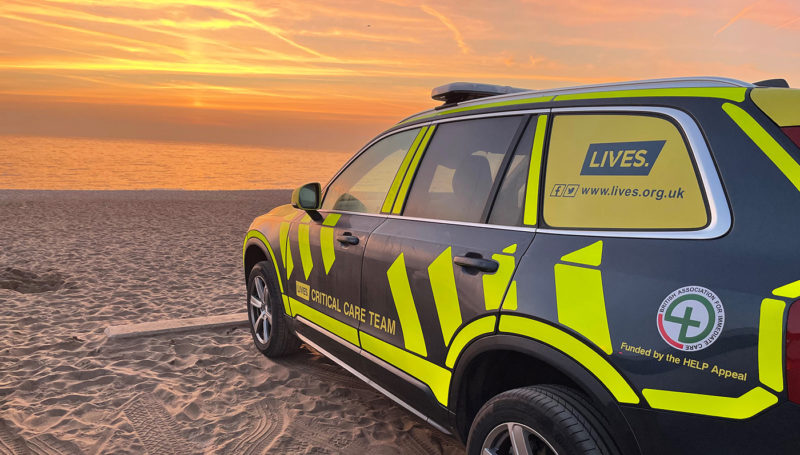 The LIVES Critical Care Car on a beach at sunrise, with reflective yellow stripes and logos