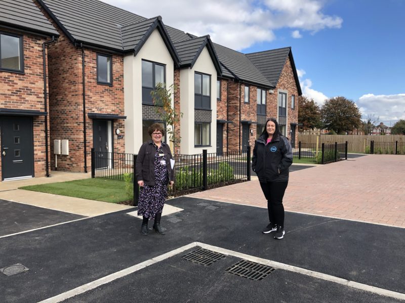 Two women posing on a new street built by social housing developers Ongo, with dark tarmac road and brick car parking