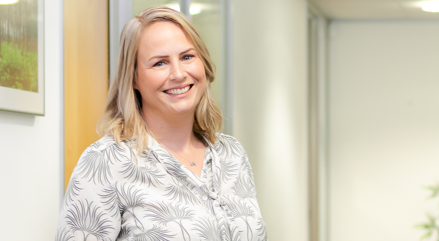 Emma Lawler, a blonde woman wearing white shirt, smiling at the camera in office environment