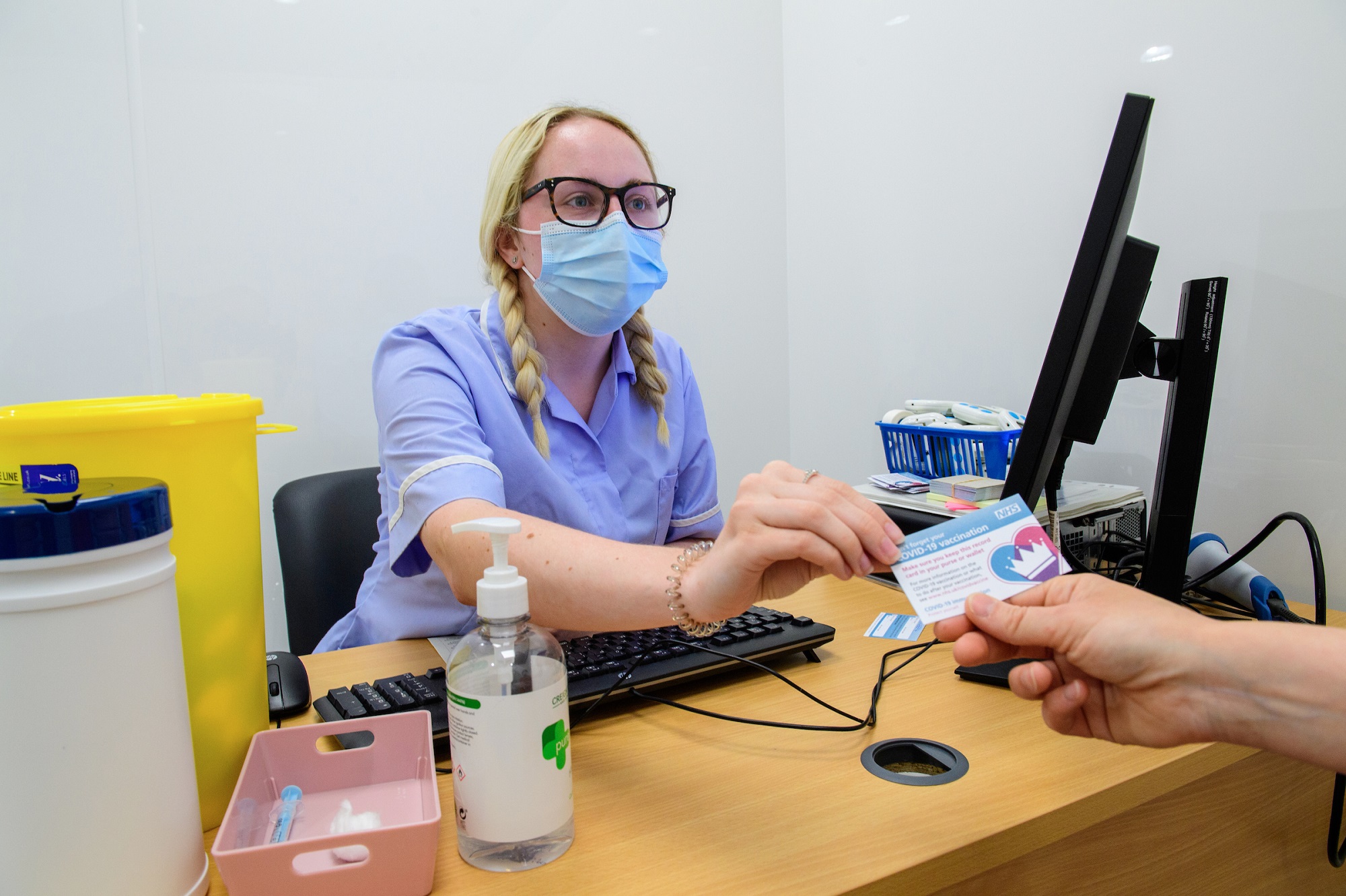 Lincolnshire Co-op’s Newland Pharmacy, Lincoln, being used as an NHS Covid-19 Vaccination Centre. Blonde nurse at desk giving vaccination card to patient