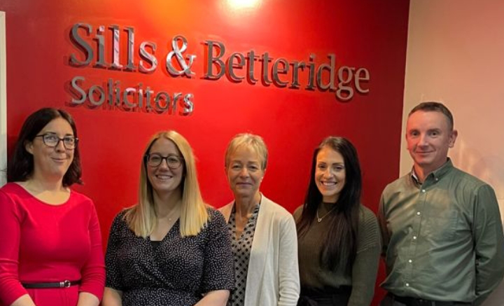 Group of men and women standing in front of red wall with Sills & Betteridge logo