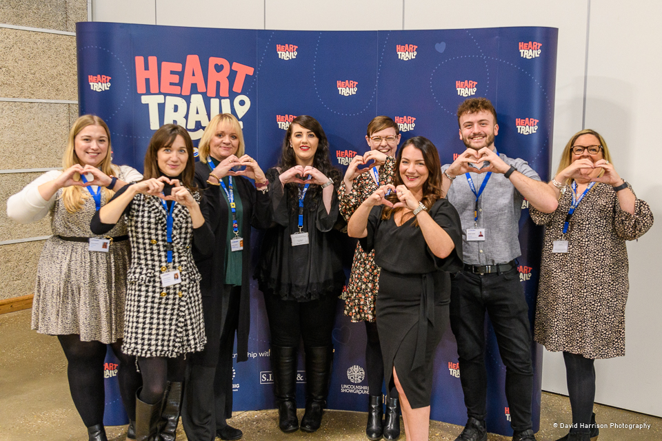 Group of people making heart shapes with their hands in front of banner