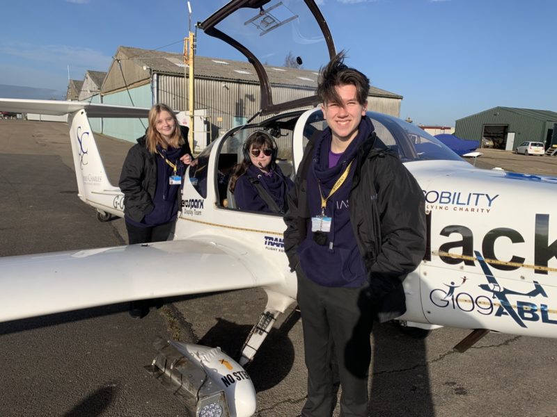 Three young students of IASTI Newark in and around a small acrobat airplane, smiling