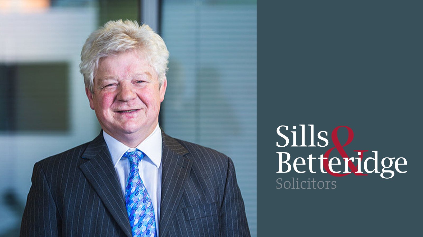 Martin Walsh, Partner at law firm Sills and Betteridge, a man with white hair, black suit jacket and blue tie, with grey background and company logo