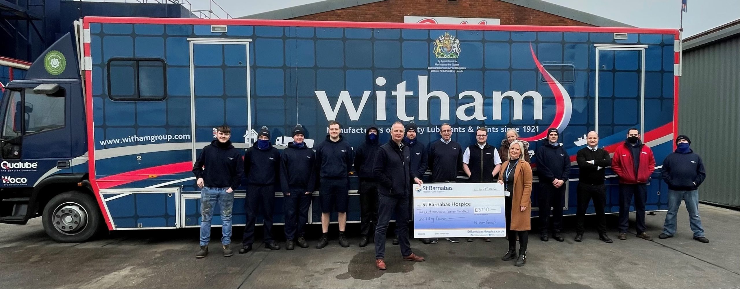 Group of men and a woman in front of lorry with Witham Group branding, holding a large cheque for St Barnabas Hospice charity