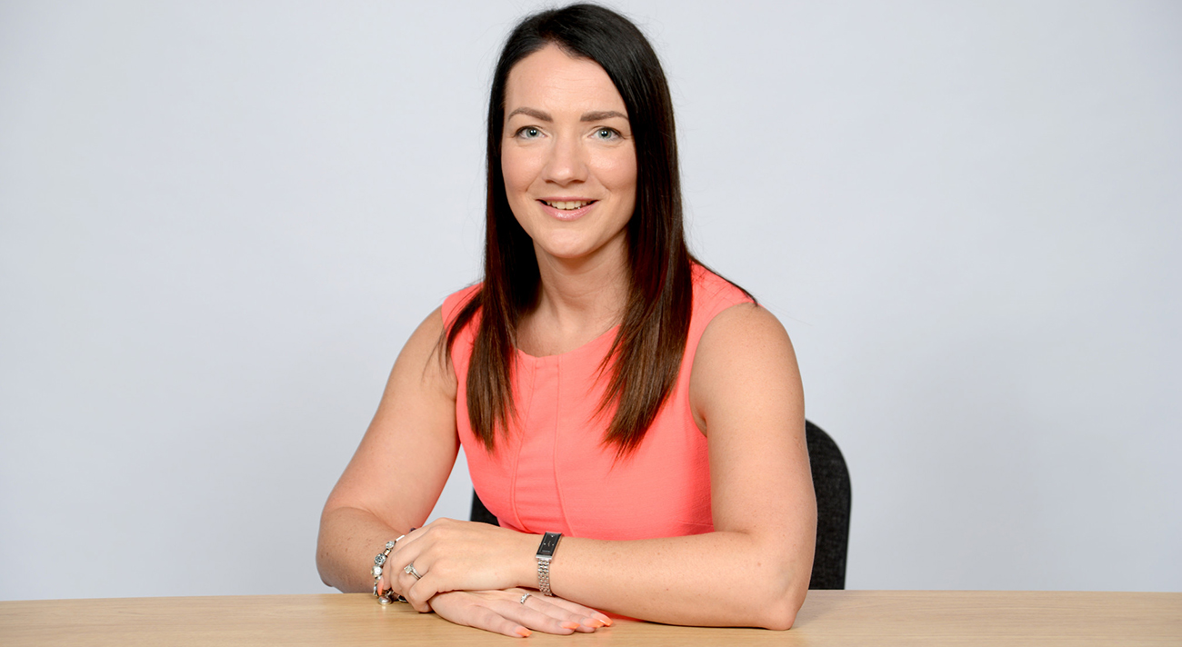 Veronica McBain from St Barnabas Hospice. Woman with long dark hair, pink sleeveless top, sitting at a table