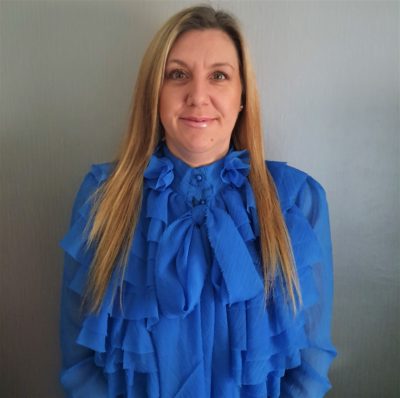 white female with mousey hair in a blue ruffle blouse against a grey background