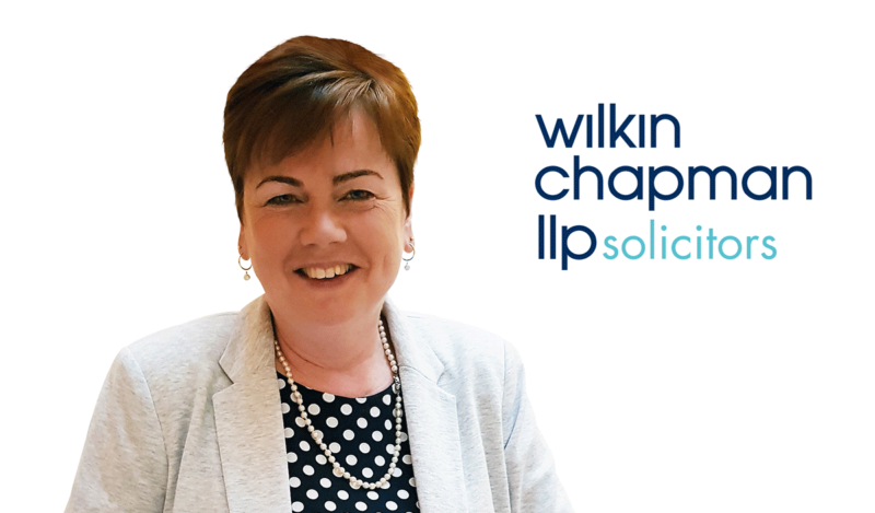 Woman with short auburn hair, white blazer and polkadot top on white background with Wilkin Chapman LLP Solicitors logo