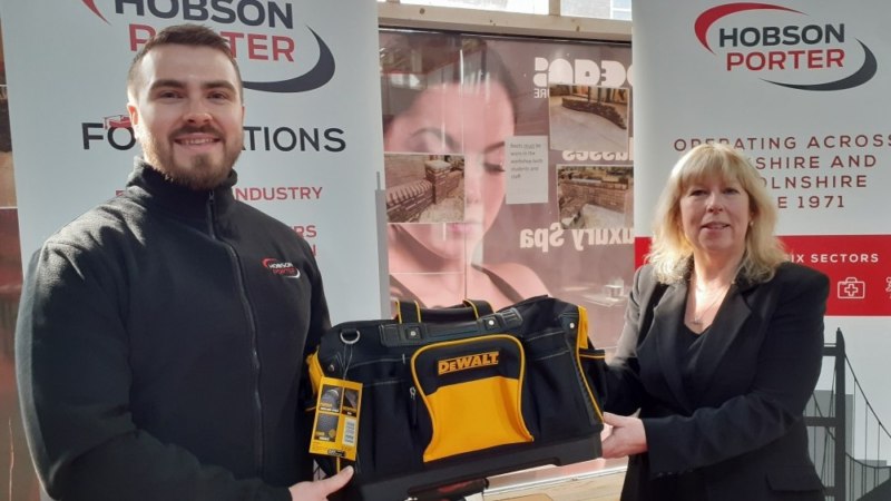 Man and woman at exhibition with Hobson & Porter banners, holding black and yellow tool kit