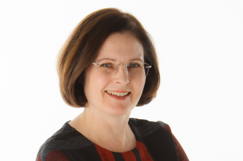 Ursula Lidbetter, a woman with dark hair, wearing glasses and a polkadot black top, smiling