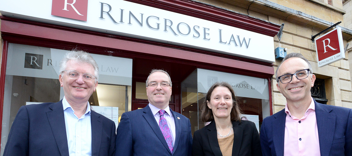 Three men and a woman in business attire outside the Ringrose Law office in Lincoln