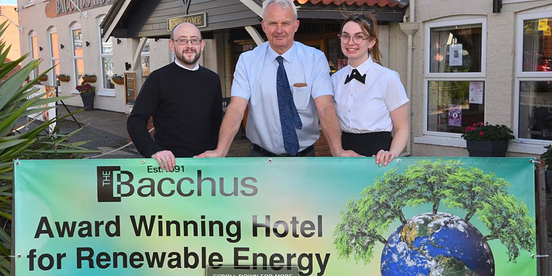 Two men and young woman holding banner with Earth and trees, black text "Bacchus award winning hotel for renewable energy"