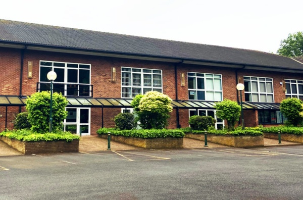 Exterior of a red brick office building with black roof and greenery