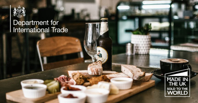 Table with tapas including bread, meats and dips, coffee in black cup, bottle of beer and glass. White logo for Department for International Trade and Made in the UK logos