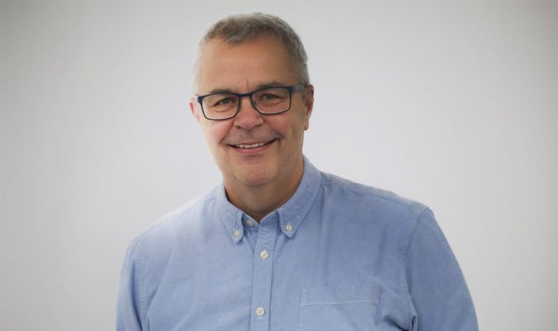 White male wearing black glasses and light blue button up shirt on grey background