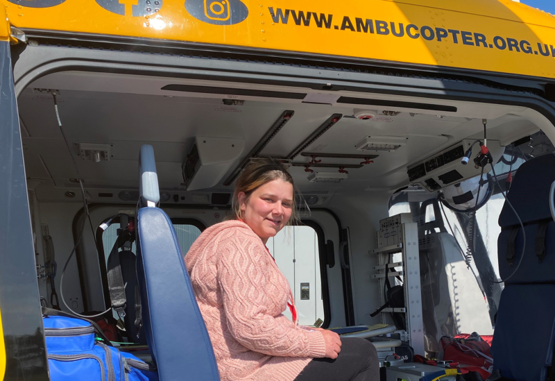 Blonde white woman wearing pink top and black leggings sitting in a yellow ambucopter.