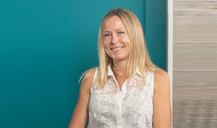 Phillippa Sturdy, a blonde female wearing a sleeveless white top and dark trousers, on teal background.