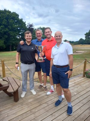 4 people standing in front of a golf course with a large trophy.