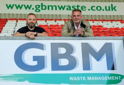 Two men, smiling, looking at the camera. They are located in a football stadium.
