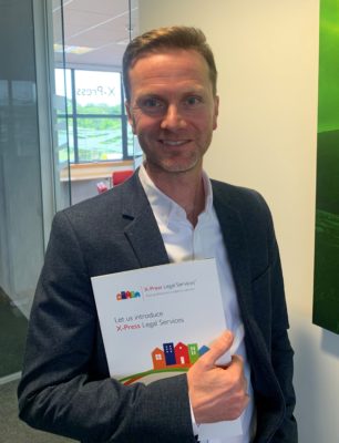 A smartly dressed man in an office looking at the camera while holding a notepad.