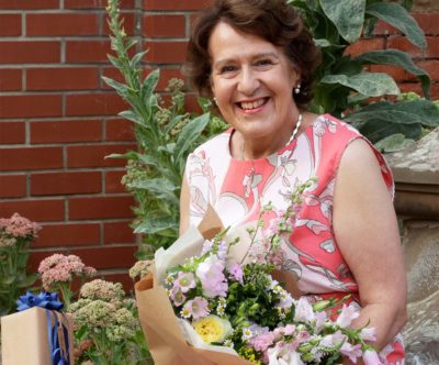 A woman, outside holding flowers, smiling at the camera.