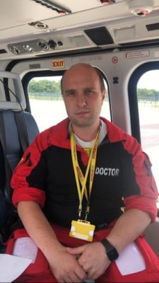 A man wearing a black and red sweater and yellow lanyard, sitting in a helicopter