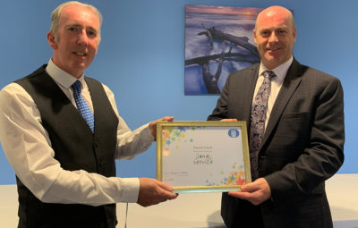 Two men, both dressed smartly, holding a Long Service certificate