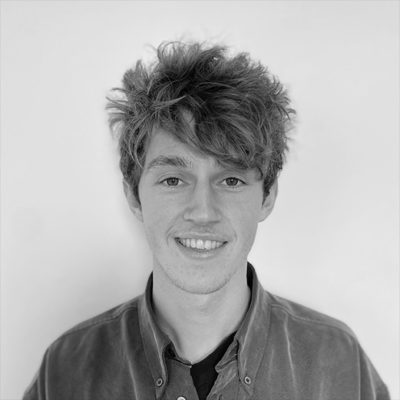 A black and white image of a male with medium-length hair, smiling at the camera